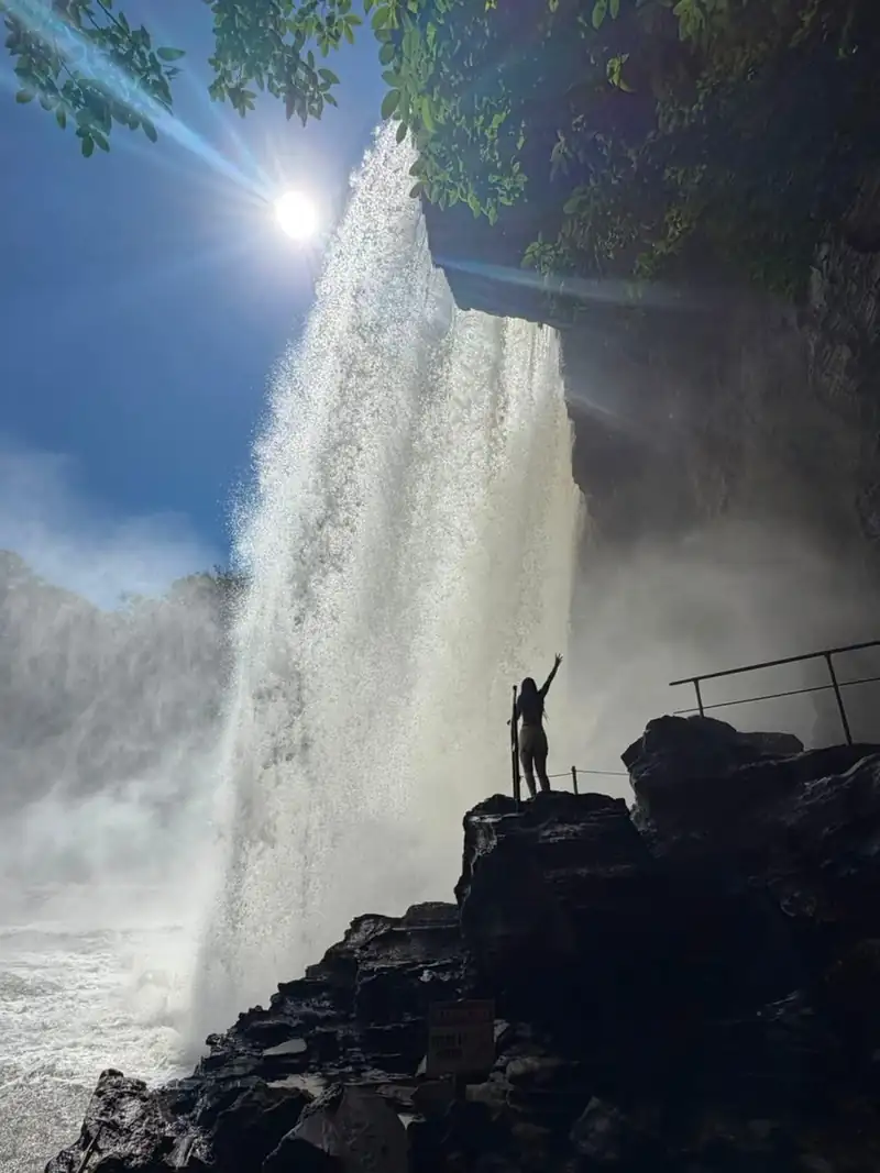 Viajante de braços abertos diante de uma grande cachoeira na Chapada das Mesas