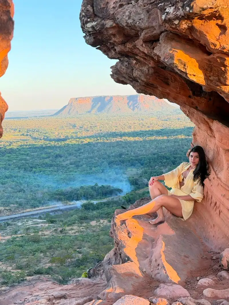 Viajante sentada na rocha com vista para a mesa da Chapada no pôr do sol