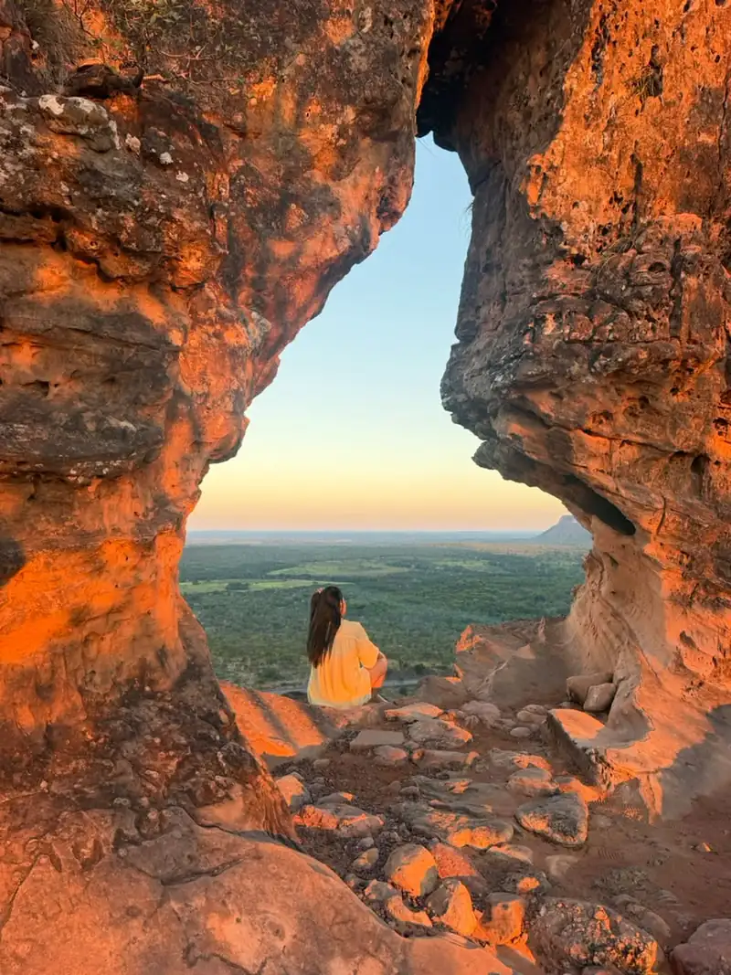 Viajante sentada no Portal da Chapada olhando o cerrado e a mesa ao pôr do sol